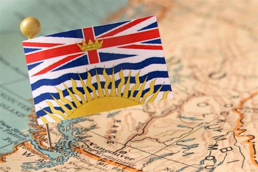 A tiny flag of British Columbia pinned on a map of the province.