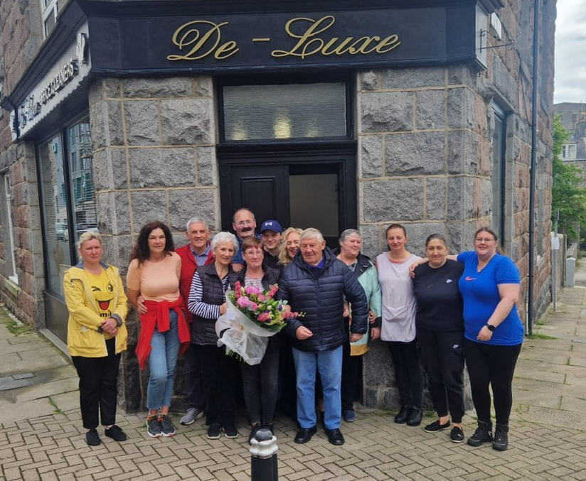 A team of people standing in front of a business called De Luxe