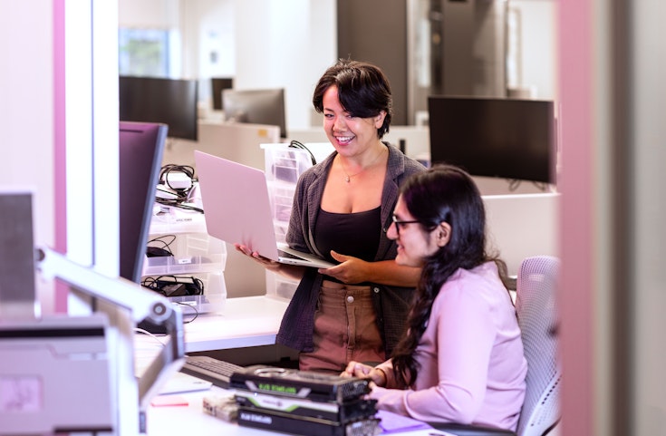 Two Ai2 team members talking, one holding a laptop.