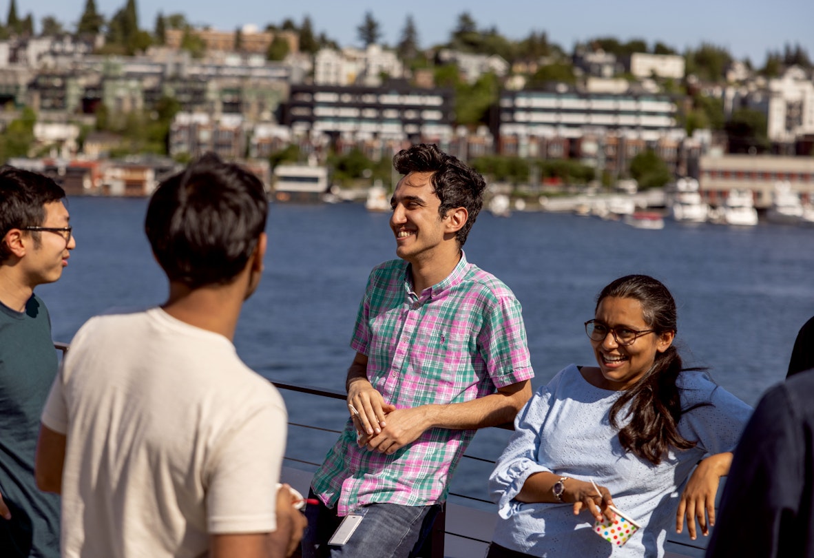 A group of Ai2 interns laughing and talking on a roof deck overlooking Lake Union.