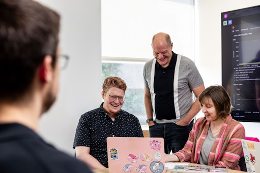 A group of Ai2 employees in a meeting, looking at a laptop screen together and laughing.