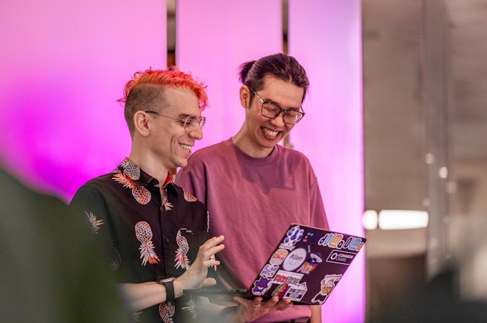 Two Ai2 team members standing looking at a laptop one of them is holding, smiling.