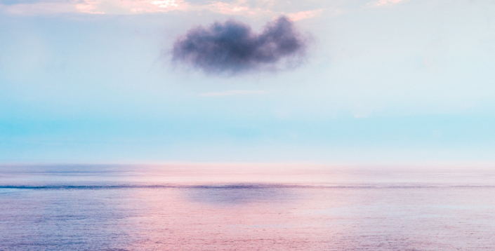 A dark cloud floats over a pastel colored sea.