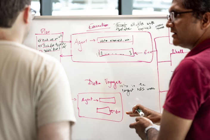 Two Ai2 team members discuss an architecture diagram drawn on a whiteboard.