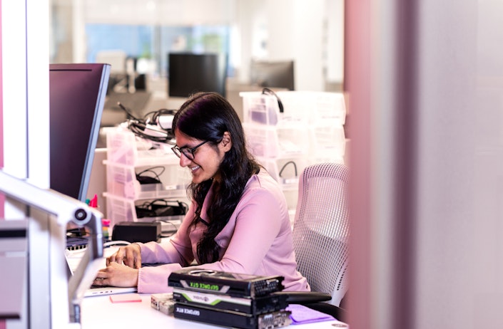 A woman works at a desk, surrounded by equipment.