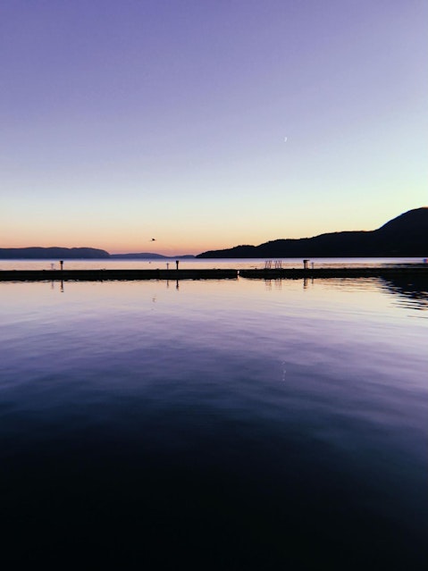 A sunset behind mountains, with a vast body of water in front.