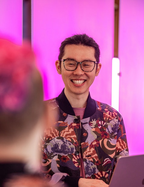 Man with glasses smiling and holding a laptop.