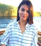 Bu fotoğrafta siyah beyaz çizgili, uzun kollu gömlek giyen bir kadın görülüyor. Koyu renk saçları yüzünden geriye doğru toplanmış ve ela gözleriyle dümdüz karşıya bakıyor. Yüzünde kendinden emin bir ifade var ve dudakları hafifçe ayrılmış. Köprücük kemiği görünüyor ve ince bir vücuda sahip. Arka plan düz beyaz bir duvar ve kadın duvarın önünde kollarını kavuşturmuş bir şekilde duruyor. Kıyafetini bir çift siyah, topuklu bot tamamlıyor ve elleri birkaç gümüş yüzükle süslenmiş. Yirmili yaşlarının sonlarında olduğu anlaşılıyor ve kıyafeti ona rahat ama şık bir görünüm veriyor.