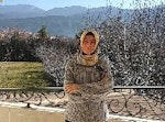 Genç bir kadın balkonda durmuş, uzaklara bakmaktadır. Beyaz bir gömlek ve koyu mavi bir kot pantolon giyiyor. Saçlarını topuz yapmış ve yüzünde sıcak bir gülümseme var. Balkon, uzakta tepelerin ve ağaçların yer aldığı huzurlu bir manzaraya bakmaktadır. Güneş batıyor ve gökyüzü turuncu, sarı ve pembenin güzel bir karışımı. Kadın ellerini korkuluklara dayamış, kendinden emin bir şekilde durmakta ve merakla dışarı bakmaktadır. O anın güzelliğine kapılmış, yüzünde neşe ve memnuniyet ifadesi var.