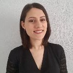 Sarı saçlı genç bir kadın kameraya mutlu bir şekilde gülümsüyor ve doğrudan objektife bakıyor. Açık ve dostça bir ifadesi var, gözleri geniş ve dudakları hafif bir sırıtış içinde. Yanakları hafifçe kızarmış ve teni ışıkta parlıyor. Beyaz bir tişört ve üzerinde küçük bir tılsım olan bir kolye takıyor. Saçları geriye doğru düşük bir at kuyruğu şeklinde toplanmış ve kolları göğsünün önünde kavuşturulmuş. Düz beyaz bir arka planın önünde duruyor ve yanında birkaç bitki var. Rahat ve memnun görünüyor, anı yaşıyor ve kamera önünde geçirdiği zamanın tadını çıkarıyor gibi görünüyor.