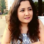 Uzun, dalgalı saçlı bir kadın kameradan uzağa bakıyor. Açık tenli ve beyaz bir tişört giymiş. Saçları ortadan ayrılmış ve uzun, tatlı bukleler halinde sırtından aşağı dökülüyor. Rahat bir ifadesi var ve dudakları hafifçe ayrılmış. Güneş ışığı saçlarındaki altın rengi röfleleri vurgulayarak güzel bir parlaklık veriyor. Arka planda ağaçların olduğu çimenlik bir alanda duruyor gibi görünüyor. Memnun ve huzurlu görünüyor.