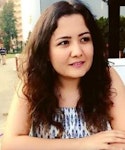 Uzun, dalgalı saçlı bir kadın kameradan uzağa bakıyor. Açık tenli ve beyaz bir tişört giymiş. Saçları ortadan ayrılmış ve uzun, tatlı bukleler halinde sırtından aşağı dökülüyor. Rahat bir ifadesi var ve dudakları hafifçe ayrılmış. Güneş ışığı saçlarındaki altın rengi röfleleri vurgulayarak güzel bir parlaklık veriyor. Arka planda ağaçların olduğu çimenlik bir alanda duruyor gibi görünüyor. Memnun ve huzurlu görünüyor.