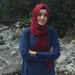 Boynuna parlak kırmızı bir başörtüsü bağlamış bir kadın kameraya bakıyor. Koyu renk gözleri uzun siyah kirpikleriyle çerçevelenmiş ve yüzünde ciddi bir ifade var. Hafif bir kumaştan yapılmış olan eşarp omuzlarından ve göğsünden aşağıya yumuşak bir şekilde düşüyor. Saçları yüzünden geriye doğru toplanmış ve kollarını önünde kavuşturmuş bir şekilde duruyor. Kendinden emin ve kararlı görünüyor, karşısına ne çıkarsa çıksın üstesinden gelmeye hazır.
