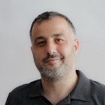 Sakallı ve bıyıklı bir adam kameraya bakmaktadır. Adamın yüzünün yanlarına doğru uzanan, düzgünce bakımlı, kalın ve koyu renk bir sakalı var. Bıyığı da kalın ve koyu renkte olup uçları hafifçe yukarıya dönüktür. Yoğun bir bakışa sahip ve gözleri sakalları tarafından çerçevelenmiş. Koyu renkli bir gömlek giyiyor ve yüzünde ciddi bir ifade var.