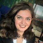 Genç bir kadın beyaz dişlerini göstererek kameraya doğru gülümsüyor. Parlak kahverengi gözleri ve yüzünden geriye doğru toplanmış uzun, siyah saçları var. Beyaz yakalı ve manşetli mavi bir gömlek ve beyaz bir etek giyiyor. Kollarını göğsünün önünde kavuşturmuş ve kendinden emin bir duruşu var. Yüzü yandan gelen ışıkla aydınlanmakta, sıcak ve davetkâr bir atmosfer yaratmaktadır. Rahatlamış ve mutlu bir halde görünüyor.
