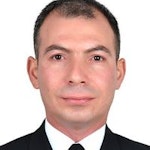 Bu, profesyonel bir ortamda duran iyi giyimli bir adamın görüntüsüdür. Beyaz gömlekli siyah bir takım elbise giymekte ve desenli bir kravat takmaktadır. Saçları düzgünce taranmış ve yüzünde ciddi bir ifade var. Bir eli cebinde, diğer eli yanında, sade bir arka planın önünde duruyor. Kendinden emin ve başarılı görünüyor. Duruşu kendinden emin ve kararlı görünüyor. Doğrudan kameraya bakıyor, bu da çevresinin farkında olduğunu gösteriyor. Bu adam güç ve sofistike bir hava yayıyor ve muhtemelen alanında önemli bir figür.