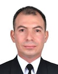 Bu, profesyonel bir ortamda duran iyi giyimli bir adamın görüntüsüdür. Beyaz gömlekli siyah bir takım elbise giymekte ve desenli bir kravat takmaktadır. Saçları düzgünce taranmış ve yüzünde ciddi bir ifade var. Bir eli cebinde, diğer eli yanında, sade bir arka planın önünde duruyor. Kendinden emin ve başarılı görünüyor. Duruşu kendinden emin ve kararlı görünüyor. Doğrudan kameraya bakıyor, bu da çevresinin farkında olduğunu gösteriyor. Bu adam güç ve sofistike bir hava yayıyor ve muhtemelen alanında önemli bir figür.