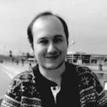 Bu, yüzünde kocaman, içten bir gülümseme olan bir adamın fotoğrafı. Mavi ve beyaz çizgili bir tişört giyiyor ve saçları koyu renk ve kısa. Yanakları hafif pembe, gözleri parlak ve neşeli. Elleri ceplerinde, beyaz bir duvarın önünde duruyor. Yüz ifadesi neşe ve memnuniyet dolu. Rahatlamış görünüyor ve güven ve rahatlık havası yayıyor. Gülümsemesi bulaşıcı ve dünyayı ele geçirmeye hazır görünüyor.
