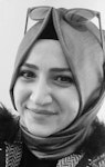 Resimdeki kadın, omuzlarından sarkan ve göğsünü örten beyaz ve mavi desenli bir eşarp takıyor. Kahverengi saçlarını arkaya toplamış ve kendinden emin bir ifadeyle dümdüz karşıya bakıyor. Gözleri kahverengi ve teni açık renk. Beyaz bir üst ve mavi kot pantolon giyiyor. Boynunda tek mavi taşlı bir kolye var. Resmin arka planı açık mavi ve gri karışımı. Kadın, uzakta birkaç ağacın bulunduğu açık bir alanda duruyor.