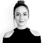 Bu, siyah gömlek giymiş bir kadının fotoğrafıdır. Beyaz bir duvarın önünde, kolları iki yanında duruyor. Yüz ifadesi nötrdür. Saçları yüzünden uzakta toplanmış ve siyah renkte. Üzerinde bol kesim, yakalı ve önden düğmeli siyah bir gömlek var. Gömlek açık mavi kot pantolonunun içine sokulmuştur. Siyah ayakkabılar giyiyor ve omzuna siyah bir çanta asmış. Işık doğal, yüzünde ve giysilerinde gölgeler yaratıyor. Kendinden emin ve bulunduğu ortamda rahat görünüyor.