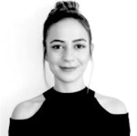 Bu, siyah gömlek giymiş bir kadının fotoğrafıdır. Beyaz bir duvarın önünde, kolları iki yanında duruyor. Yüz ifadesi nötrdür. Saçları yüzünden uzakta toplanmış ve siyah renkte. Üzerinde bol kesim, yakalı ve önden düğmeli siyah bir gömlek var. Gömlek açık mavi kot pantolonunun içine sokulmuştur. Siyah ayakkabılar giyiyor ve omzuna siyah bir çanta asmış. Işık doğal, yüzünde ve giysilerinde gölgeler yaratıyor. Kendinden emin ve bulunduğu ortamda rahat görünüyor.
