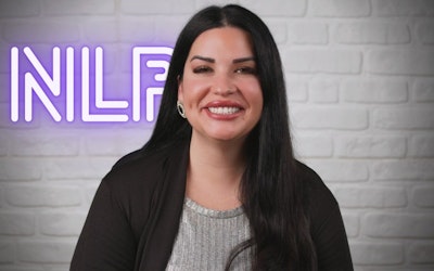 This image shows an online Neuro-Linguistic Programming (NLP) certification and online course. Against a grey background is a neon purple NLP sign highlighting the focus of the course. An expert NLP trainer, dressed in a grey blouse and black cardigan, signifies the professional training that students will receive. The image promotes the comprehensive NLP course, delivered through online courses, leading to certification. It represents the opportunity to learn NLP and become a certified practitioner through an accessible, online platform. As can be seen from the image, the course includes training and certification in Neuro-Linguistic Programming. Overall, it is clear that this is an online course that teaches valuable skills.