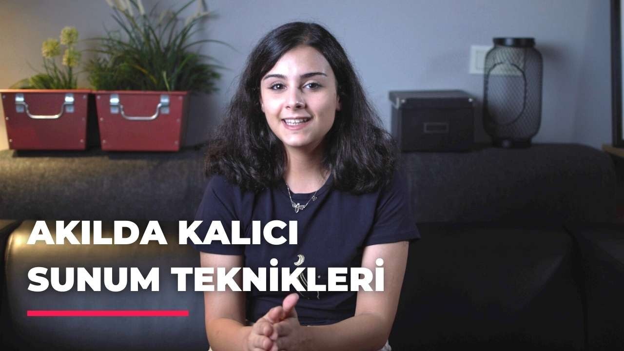 Uzun, siyah saçlı bir kadın kahverengi bir kanepede rahatça oturuyor. Mavi bir gömlek giymiş ve mutlu bir şekilde gülümsüyor. Arkasında bir çitin bulanık görüntüsü ve sakallı bir adam saksıda bir bitki tutmaktadır. Kadının solunda bir bitkinin bulanık bir görüntüsü ve kırmızı bir kutunun yakın çekimi yer alıyor. Kadın, sıcak tonlar ve doğal unsurlarla çevrili ortamında memnun ve rahat görünüyor.