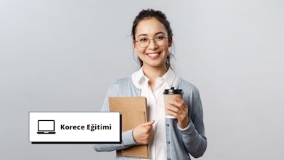 Gözlüklü bir kadın elinde bir kahve fincanı ve bir defter tutarken gülümsüyor. Defter açık ve kadın dikkatle yere bakıyor, elindeki işe odaklanıyor. Kahve fincanı beyaz, sapı koyu kahverengi ve defterin üzerine gri bir örtü örtülmüş. Arkasındaki duvar düz beyazdır ve arka planda kahverengi bir karton üzerine yazılmış siyah bir metin vardır. Kadın rahat bir kıyafet giymiş ve yüzü hoş bir ifadeyle aydınlanmış. Gözleri kararlılıkla odaklanmış ve o anda yapmakta olduğu faaliyete dalmış durumda.