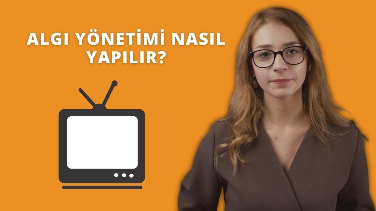 Gözlüklü ve kahverengi gömlekli bir kadın siyah turuncu televizyonun önünde duruyor. Yüzünde ciddi bir ifadeyle doğrudan kameraya bakıyor, gözleri gözlüklerinin yuvarlak çerçeveleriyle çerçevelenmiş. Kahverengi gömleğinin düğmeleri sonuna kadar iliklenmiş ve açık mavi kot pantolonunun içine sokulmuştur. Dudakları hafifçe ayrılmış ve saçları düşük bir at kuyruğu şeklinde geriye doğru toplanmış. Kadının arkasında kalın harflerle Hoş geldiniz yazılı siyah ve turuncu bir tabela var. Sahne sarı bir arka planla çerçevelenmiştir.