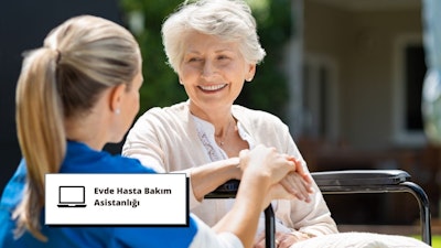 Bu resimde el ele tutuşan ve biri gülümseyen iki kadın görülüyor. Bir hasta ile evde hasta bakım asistanı arasındaki önemli bağın mükemmel bir örneği. Arka plandaki mavi beyaz tabela, kurs hakkında yardımcı bir metin sunarak bunun bir eğitim programı olduğunu gösteriyor. Kadının gülümseyen yüzünün yakın çekimi de evde hasta bakımında şefkat ve anlayışın önemini anlatıyor. Kadının diğer kadınınkini tutan ellerinin yakın çekimi, ihtiyaç duyulan fiziksel bakım ve desteği gösteriyor. Boynunun ve at kuyruğu yapılmış saçlarının yakın çekimi hastanın rahat ve güvende olduğunu gösteriyor. Arka plandaki adam bize evde hasta bakım asistanlarının içinde çalıştığı daha geniş bir topluluğu hatırlatıyor. Tüm bu unsurlar bir araya gelerek evde hasta bakım asistanı eğitiminin önemini aktaran güçlü bir görüntü oluşturuyor.