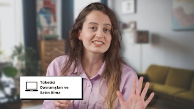 Bir kadın kapalı bir odada ayakta durmakta ve elinde bir tabela tutmaktadır. Gülümsüyor, açık renkli bir kıyafet giyiyor ve yüzü yakın planda. Elindeki tabela beyazdır ve üzerinde siyah yazılar vardır. Arkasında bir duvar ve aralarında bir kanepenin de bulunduğu bazı mobilyalar var. Eli de yakın plandadır ve arkasında bulanık bir arka plan vardır. Kameraya bakıyor, yüz ifadesinde güven ve neşe var. Duruşu rahattır ve rahat bir ortamdaymış gibi görünür. Saçları arkaya toplanmış ve cildi parlıyor. Elindeki pankart boş ama onu inançla tutuyor.