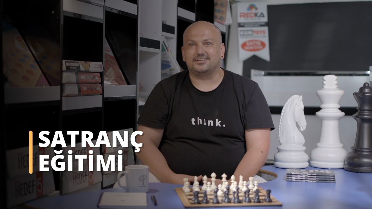 Bir adam önünde satranç tahtası olan bir masada oturmaktadır. Gömlek ve pantolon giymiştir ve yüzü görünmektedir. Önündeki satranç taşlarına dikkatle konsantre olmuş, bakışları satranç tahtasına odaklanmıştır. Masanın üzerinde, üzerinde ağaç resmi olan beyaz bir kupa ve bir yığın bilgisayar klavyesi vardır. Sağında, biri beyaz diğeri metal olmak üzere birkaç satranç taşı var, ikisi de yakından bakıyor. Arkasındaki duvarda üzerinde yazı olan bir tabela var. Odaklanmış ve kararlı görünüyor, hamle yapmaya hazır.