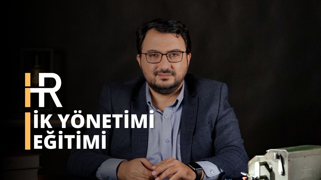 Bu görüntü, masa başında muhtemelen bir İnsan Kaynakları Yönetimi kursuna katılan bir adamı yakalıyor. Gözlüklü ve takım elbiseli adamın yakın çekimde gözleri, saati ve gömleği görülüyor. Gözlüklü ve sakallı yüzü görülüyor. Gömleğinin kolu da görülebiliyor. Masada metal bir kutu bulunmaktadır. Bu görüntü, İK sertifikasyon kurslarının önemini ve profesyonellerin bu alanda mükemmelleşmek için ihtiyaç duydukları beceri ve bilgileri kazanmalarına nasıl yardımcı olabileceklerini ideal bir şekilde temsil etmektedir. İK sertifikası, işverenlere çalışanlarının işi yapmak için gerekli niteliklere sahip olduğuna dair güven verir. Ayrıca iş arayanlara da seçtikleri meslekte mükemmelleşmek için doğru becerilere sahip olduklarına dair güvence sağlar.