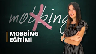 Bir kadın kara tahtanın önünde duruyor. Kollarını kavuşturmuş ve yüzünde şaşırtıcı derecede sıcak bir gülümseme var. Uzun, siyah saçları arkaya toplanmış ve üzerinde rahat, açık renkli bir gömlek var. Kara tahtanın üzerinde beyaz bir metin ve farklı renklerde birkaç şekil ve diyagram yazılı. Kadın kendinden emin ve memnun görünüyor, önündeki tahtada yazılı olan bilgileri bir an için kavrıyor. Görüntü kara tahtanın yakın çekimidir ve metnin ve diyagramların karmaşık ayrıntılarını göstermektedir. Kadının varlığıyla çerçevelenen genel kompozisyon, çevreye benzersiz bir bakış açısı sağlıyor.