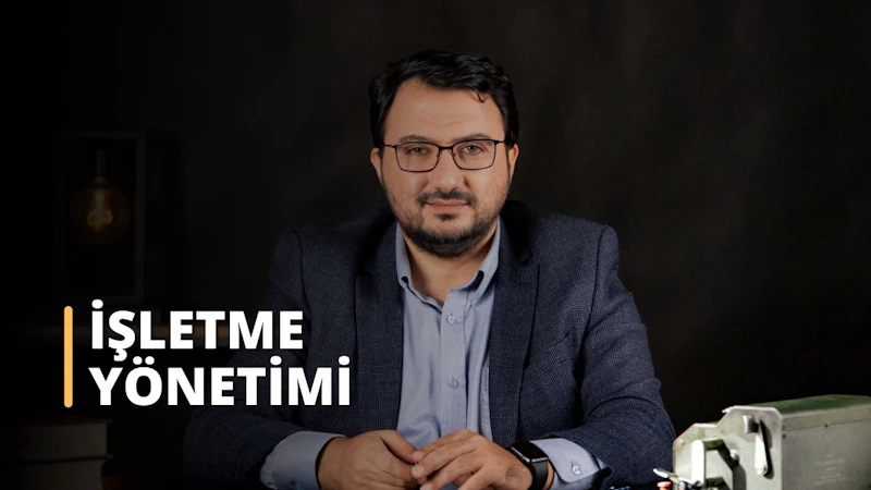 Bu resimde masa başında oturan, gözlüklü ve takım elbiseli bir adam görülüyor. Masanın üzerindeki metal kutudan ve muhtemelen bir zaman yönetimi aracı olarak kullanılan saatin yakın çekiminden de anlaşılacağı üzere, muhtemelen bir iş yönetimi eğitim kursuna katılıyor. Yüzü de yakından görülüyor ve düğmeli gömleği profesyonel bir atmosfere işaret ediyor. Bu görüntü, iş yönetimi eğitiminin önemini göstermek için mükemmeldir. Görevlerin üstesinden gelmek ve öncelikleri belirlemek için doğru araçlarla kendini hazırlamanın ve profesyonel bir imaj sergilemenin önemini vurguluyor. İşyerinde başarı için iş yönetimi eğitimi şarttır.