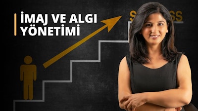 Siyah elbise giymiş koyu renk saçlı bir kadın, siyah zeminli bir kara tahtanın önünde duruyor. Kollarını kavuşturmuş, gülümsüyor ve uzun saçları omuzlarına dökülüyor. Kara tahtanın üzerinde bir merdiveni gösteren sarı bir ok var ve beyaz tebeşirle bir grafik çizilmiş. Kadının sağ eli dirseğine dokunmaktadır. Kara tahtanın sağ alt köşesinde sarı ve siyah bir işaret, onun üzerinde de siyah zemin üzerine sarı bir harf var.