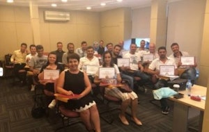 A group of diverse people in formal attire are in a celebration mood. They are all holding certificates and have huge smiles on their faces. The certificates are brightly colored and have different designs and lettering. Everyone in the group is wearing formal suits and dresses. The vibrant atmosphere is full of joy, pride, and accomplishment. They are standing proudly, celebrating their achievements and recognizing the efforts that led to their success.