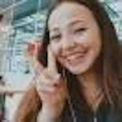 Yüzünde parlak ve neşeli bir gülümseme olan bir kadın, sanki heyecanla birine bir şey gösteriyormuş gibi kolunu uzatmış yukarı doğru işaret ediyor. Omuz hizasında kahverengi saçları var ve beyaz bir tişört giyiyor. Gözleri geniş ve parlak, dudakları sırıtarak hafifçe ayrılmış. Yüzü neşe ve mutluluk saçıyor ve çok iyi bir ruh hali içinde gibi görünüyor. İfadesi iyimserlik dolu ve duruşu kendinden emin ve iddialı. Kolunu, gülümsemesiyle ilettiği neşe duygusunu vurgulayacak şekilde yukarı kaldırmış.