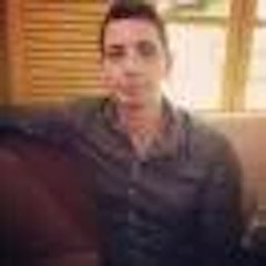 Genç ve yetişkin bir adam kanepede rahat bir pozisyonda oturuyor. Kollarını hafifçe kolçaklara dayamış ve bacak bacak üstüne atmış. Üzerinde beyaz bir tişört ve mavi bir kot pantolon var. Gözleri derin düşüncelere dalmış ya da sadece anın tadını çıkarıyormuş gibi kapalı. Kahverengi saçları düzgünce taranmış ve yüzünde belli belirsiz bir gülümseme var. Oturduğu kanepe koyu mavi kumaştan ve açık gri duvarları ve beyaz mobilyaları olan bir odada yer alıyor. Odada tül perdeli tek bir pencere ve etrafa dağılmış birkaç bitki var. Genel atmosfer huzurlu ve sakinleştirici.
