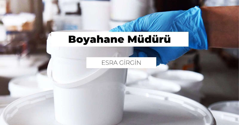 Beyaz bir kova tutan mavi eldivenli bir elin yakın plan görüntüsü. Kovanın sapı net bir şekilde görülebiliyor ve eldivenin dokusu görülebiliyor. Ayrıca elin yanında siyah beyaz bir logo ve ortasında beyaz bir daire olan küçük siyah bir daire var. Kovanın yanı sıra, arka planda hafif bir bulanıklıkla beyaz bir fincan da görülebiliyor. Ayrıca, görüntünün alt kısmında bir kişinin yüzünün küçük bir kısmı görülebiliyor. İfade net değil, ancak cildin renkleri hala görülebiliyor.