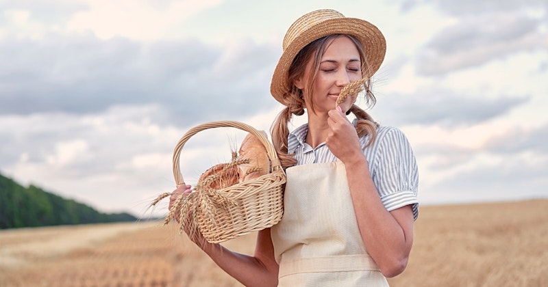Hasır şapka takmış bir kadın elinde yeni pişmiş ekmek sepeti tutuyor. Arka planda ağaçların olduğu uzun otlarla kaplı bir tarlada duruyor. Güneş ışığı kadının yüzünde parlıyor ve güzel, altın rengi bir ton yaratıyor. Sepet ekmekle dolu, somunların bazıları hâlâ demet halinde. Kadın gülümsüyor ve yüzünde huzurlu bir ifadeyle halinden memnun görünüyor. Saçları düzgün, düşük bir topuz şeklinde geriye toplanmış ve elbisesi basit ve sade. Tarla yemyeşil ve gökyüzü parlak bir mavidir. Kadının sıcak, davetkâr bir duruşu var ve etrafı dingin bir atmosferle çevrili.
