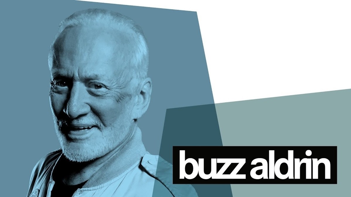 Kalın, siyah sakallı bir adam gözlerini hafifçe kısmış, dosdoğru karşıya bakıyor. Saçları kısa ve düzgünce kesilmiş. Düz beyaz bir tişört giymektedir ve arka planda beyaz harflerle siyah beyaz bir tabela vardır. Adamın güçlü bir çene hattı var ve yüzünün yakın çekimi genç ten rengini ortaya koyuyor. Kameraya doğru bakarken yüzünde ciddi bir ifade var. Görüntü kararlılık ve güç hissi uyandırıyor.