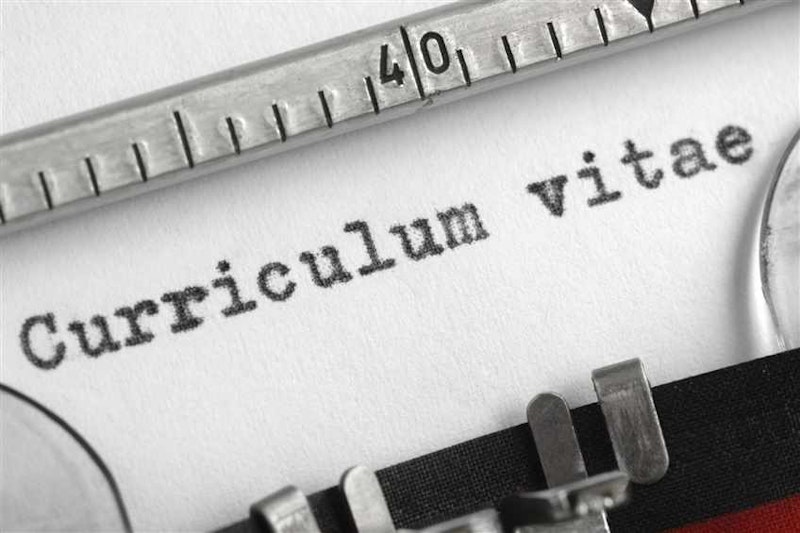 Bu yakın çekim görüntü bir daktilo ve metal bir cetvele aittir. Daktilo metal ve siyah renkli bir makinedir, klavyesinde bir dizi tuş vardır ve makineye beyaz bir kağıt yerleştirilmiştir. Cetvel de metaldir ve düz, dikdörtgen bir şekle sahiptir. Üzerinde bir dizi küçük çizgi ve ölçü işaretlenmiştir. Resmin sol tarafında, masanın üzerinde bir bardak su var. Su berrak görünüyor ve suyun yüzeyinde daktilo ve cetvelin bir yansıması var. Görüntü keskin bir odağa sahiptir ve daktilo ile cetvelin ayrıntıları net bir şekilde görülebilmektedir.