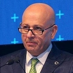 Takım elbiseli adam yüzünde ciddi bir ifadeyle dimdik ayakta duruyor. Açık mavi takım elbisesi tam oturmuş ve aynı derecede net beyaz bir gömlek ve koyu mavi kravatla tamamlanmış. Saçları düzgünce geriye taranmış ve gözleri uzaktaki bir şeye odaklanmış. Parlatılmış siyah deri elbise ayakkabıları giyiyor. Elleri önünde birbirine kenetlenmiş ve bir şey bekliyor gibi görünüyor. Duruşu kendinden emin ve ağırbaşlı, profesyonellik ve yetkinlik havası taşıyor. Önüne çıkan her türlü zorluğun üstesinden gelmeye hazır görünüyor.