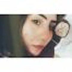 Bu görüntüde akıllı telefon kamerasıyla selfie çeken genç bir kadın görülüyor. Açık mavi bir tişört giyiyor, saçlarını topuz yapmış ve yüzünde ciddi bir ifade var. Beyaz duvarları ve sağda bir penceresi olan bir odada duruyor. Sağ elinde telefonu yüzünün önünde tutuyor ve sol eli görüntünün köşesinde görülebiliyor. Kendinden emin ama ciddi bir duruşu var ve pencereden gelen ışık yüzünü aydınlatıyor. Hatırlamak istediği bir anı yakalamaya hazır görünüyor.