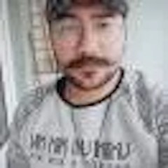 Bıyıklı ve sakallı genç bir adam selfie çekiyor. Telefonunu önünde tutuyor ve kararlı bir ifadeyle objektife bakıyor. Yüzündeki kıllar düzgün, kalın bir bıyık ve dolgun, kalın bir sakal şeklinde bakımlı. Siyah bir tişört ve koyu renk bir kot pantolon giymiş. Arka plan net değil ama kadrajda bir oturma odasının izleri var. Bu selfie'yi çekerken gözleri odaklanmış ve konsantre olmuş durumda. Anın tadını çıkarıyor gibi görünüyor ve yüzü sıcak, mutlu bir ifadeyle aydınlanıyor.