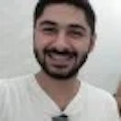 Bu, doğrudan kameraya bakan, ışıl ışıl gülümseyen bir adamın yakın plan çekimi. Gözleri parlak ve pırıl pırıl, dudakları ise davetkâr ve sıcak bir sırıtışla kıvrılmış. Hafif bir teni var ve yanaklarına birkaç çil serpiştirilmiş. Saçları kısa ve dağınık, birkaç günlük kirli sakalı var. Başı hafifçe yana eğik, bu da onu arkadaş canlısı ve cana yakın gösteriyor. Üst iki düğmesi açık beyaz bir gömlek giyiyor ve boynunu bir anlığına ortaya çıkarıyor. Duruşu rahat ve kendinden emin, bu da ona kendine güvenen bir hava veriyor. Yirmili yaşlarının sonlarında ya da otuzlu yaşlarının başında olduğu anlaşılıyor ve o anın içinde mutlu ve rahat görünüyor.