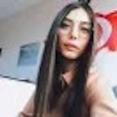 Genç bir kadın beyaz bir duvarın önünde duruyor, cep telefonunu yüzüne tutuyor ve gülümsüyor. Pembe yakalı, mavi beyaz çizgili bir gömlek giymiş, saçlarını topuz yapmış. Yanakları hafif pembe, gözleri parlak ve hayat dolu. Yirmili yaşlarının başında görünüyor ve yüz ifadesi rahat ve memnun. Bir selfie çekiyor, neşe ve memnuniyet anını yakalıyor. Telefonu sol elinde, başparmağı hafifçe deklanşör düğmesine dayanıyor. Sanki fotoğrafı çekmek üzereymiş gibi başını hafifçe eğmiş. Tüm sahne memnuniyet ve mutluluk duygusuyla dolu.