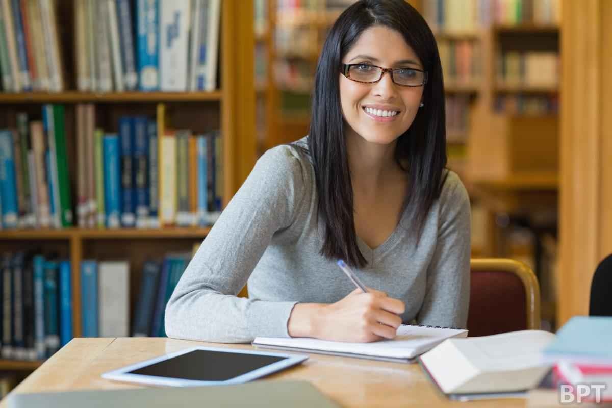 Bir kadın masada oturmuş, bir kitap yazıyor. Kadın kameraya gülümsüyor ve odak ön planda onun sandalyesinde. Arka planda bir tabletin yakın çekimiyle birlikte siyah kare bir nesne görülüyor. Ayrıca beyaz bir yüzeyin yakın çekimi ve bulanık bir kalem ve el görüntüsü de var. Uzak arka planda, bir kitap rafının ve siyah kenarlıklı beyaz bir duvarın bulanık bir yakın çekimi var. Kadın rahat ve memnun görünüyor, işine dalmış. Kadın, arka plandaki çeşitli nesnelerle çevrili görüntünün merkez odağıdır.