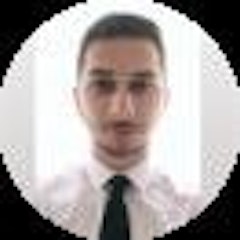 Resimdeki adam beyaz bir gömlek giymiş ve kravat takmış. Yüzünde dostça bir ifade var ve saçları düzgünce yana taranmış. Ayaklarının altında bej bir halı bulunan açık gri bir duvarın önünde elleri cebinde durmaktadır. Gömleğinin düğmeleri iliklidir ve kravatı lacivert renktedir. Siyah bir kemer ve ona uygun siyah ayakkabılar giymektedir. Yüz hatları belirgin ve yirmili yaşlarının ortalarında görünüyor. Kıyafetleriyle vurgulanan ince bir vücut yapısı vardır. Sol elinde bir saat ve gümüş bir yüzük takıyor. Varlığı sıcak ve davetkâr, kendinden emin ve bakımlı bir birey izlenimi veriyor.